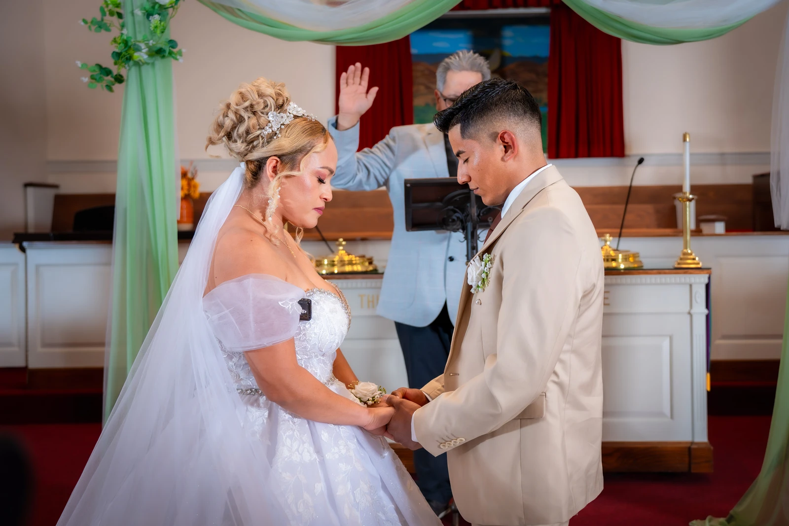 Bride and groom holding hands during wedding ceremony prayer inside church in Kansas City